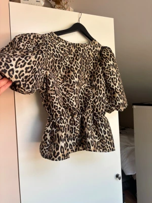 Leopardmönstrad topp med puffärm - Snygg topp med leopardmönster och puffiga korta ärmar. Modellen har markerad midja och lätt volang nedtill för en trendig siluett. 