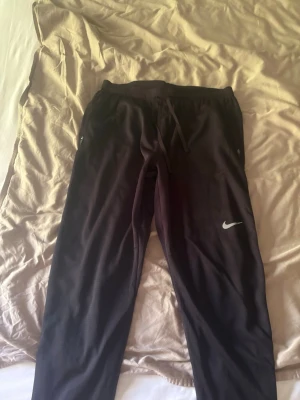 Svarta träningsbyxor  - Säljer ett par svarta byxor med dragsko i midjan och diskret logga på benet. Tillverkade i 100% polyester med Dri-FIT-teknologi som håller dig torr under träningen. Perfekta för löpning eller gymmet.