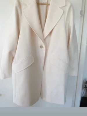 H&M offwhite oversized kappa, storlek S - En oversized stilren vår/sommar kappa i en ljus nyans med en knapp framtill och två fickor. Kappan har en klassisk krage och är perfekt för att komplettera en elegant outfit. Helt ny oanvänd. Nypris 799kr. Djur och rökfritt hem. Mått L83cm B47cm ärmlängd 59cm