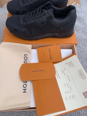 Svarta Louis Vuitton sneakers - Snygga helsvarta Louis Vuitton sneakers med monogramdetaljer på sidan. Skorna har en klassisk låg siluett, platt sula och är tillverkade i en mix av läder och textil. Perfekta för dig som vill ha en exklusiv och stilren look.