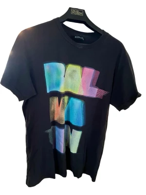 Svart Balmain t-shirt med färgglatt tryck - Cool svart t-shirt från Balmain med stort färgglatt tryck framtill i blått, grönt, gult och rosa. Klassisk rund hals och korta ärmar. Tillverkad i mjuk bomull för skön känsla och avslappnad passform. Bra skick. 