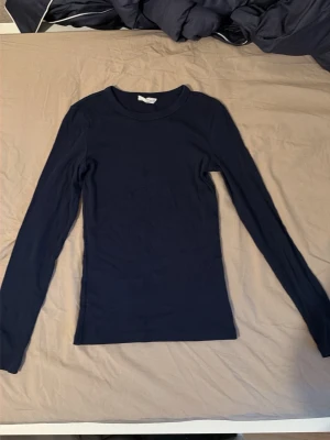 Mörkblå långärmad topp - En enkel och stilren mörkblå långärmad topp med rund hals. Toppen har en slim passform och är tillverkad i mjukt material som känns skönt mot huden. Perfekt att matcha med jeans eller kjol för en clean look.