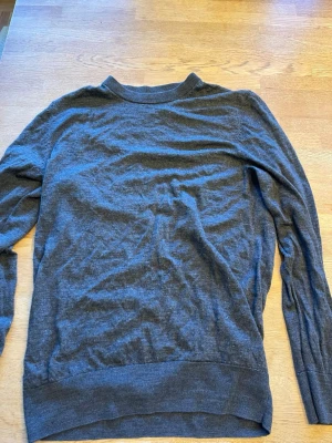 Mörkgrå stickad tröja från H&M - En enkel och stilren mörkgrå stickad tröja från H&M. Tröjan har rund halsringning, långa ärmar och ribbade muddar vid ärmslut och nederkant. Perfekt att bära över en skjorta eller t-shirt för en avslappnad look.