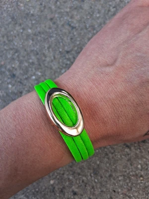 Grönt armband med metalloval - Snyggt armband i neon-grönt med flera smala band och en stor oval detalj i metall. Perfekt statement-piece för dig som vill sticka ut och addera färg till din stil.