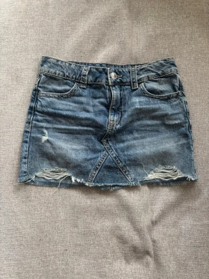 Blå jeanskjol med slitningar - Säljer en blå jeanskjol i kort modell med slitna detaljer framtill🥰