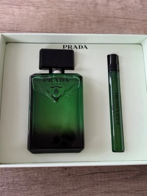 Prada Milano grön parfymset - Snyggt parfymset från Prada Milano med en större flaska och en mindre sprayflaska. Båda flaskorna är i elegant grön glasdesign med svarta detaljer och tydlig Prada-logga. Perfekt för dig som gillar exklusiva dofter och stilren design.
