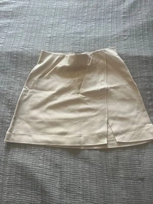 Beige omlottkjol i bomull - Snygg beige kortkjol med omlottdetalj och liten slits framtill. Kjolen har en enkel och stilren design som passar till många olika looks. Tillverkad i mjukt bomullsmaterial för en bekväm känsla.