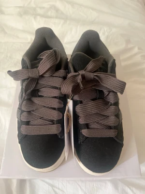Adidas Campus svarta sneakers - Säljer mina as snygga  Adidas Campus sneakers i svart mocka med klassiska tre ränder på sidan och gråa breda skosnören. Låg modell med vit sula och diskret guldfärgad 'CAMPUS'-text på sidan. Perfekta för en stilren och avslappnad look, aldrig använda då ja beställt fel storlek, de är strl 36/1.2