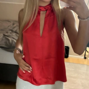Röd halterneck topp i satin - Snygg röd halterneck topp i glansigt satinmaterial med knyt i nacken och en djup v-ringning framtill. Toppen är ärmlös och har en lös passform som ger en chic och trendig look. Den är helt oanvänd!💗