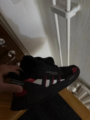 Svarta Adidas sneakers med röda detaljer - Säljer ett par svarta Adidas sneakers med klassiska vita ränder och röda detaljer. Skorna har textdetaljer på sidan och en chunky sula för en modern streetwear-look. Materialet är en mix av textil och syntet. Perfekta för dig som gillar stilrena men ändå unika sneakers.