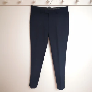 Mörkblå kostymbyxa från Bläck MQ storlek 146 - Mörkblå tunn kostymbyxa från Bläck MQ, i 60 % ull 40 % polyester. Tailored fit. Tvättbara på 40 grader. Knappt använda, mycket bra skick. Storlek 146. 