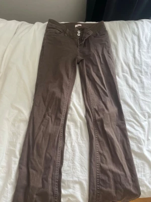 Nelly jeans  - Snygga bruna jeans med bootcut-modell och två knappar framtill. Jeansen har dekorativa sömmar på bakfickorna och klassisk femficksdesign. Tillverkade i ett mjukt bomullsmaterial som sitter skönt och ger en avslappnad look.