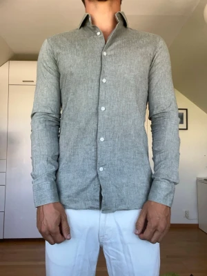 Grön/grå linneskjorta  - Grön/ grå skjorta tillverkad i 70% bomull och 30% linne från märket Nølson i strl 37 som motsvarar Small. Modellen är 178 cm och väger 77 kg. Hör gärna av dig vid frågor!