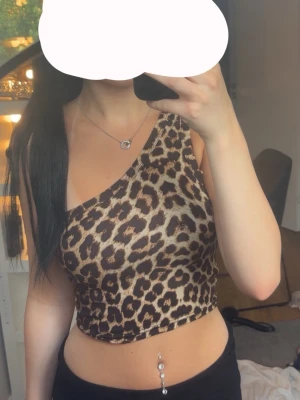 Leopardmönstrad one shoulder topp - Snygg och trendig leopardmönstrad topp med one shoulder-design. Toppens passform är tight och den är ärmlös, perfekt för att sticka ut. Materialet känns mjukt och följsamt mot kroppen.