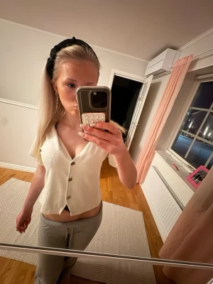 Vit  blus med knappar - Säljer en vit blus med v-ringning och korta ärmar. Toppen har tre knappar framtill och är tillverkad i ett mjukt bomullsmaterial. Perfekt för dig som gillar en enkel och stilren look.