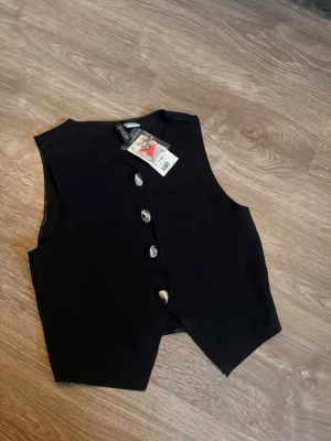 Svart väst med silvriga knappar - Svart väst/topp med silver detaljer från HM aldrig använd nypris 179kr köpt på rea för 100kr, prislapp finns kvar 