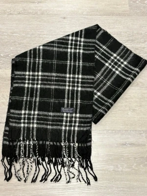 Burberry Classic Check Scarf – 100% Lambswool – Made in England - Klassisk halsduk från Burberrys i svart och vitt rutigt mönster. Tillverkad i 100% lammull och har fransar i ändarna. Perfekt accessoar för att lyfta din outfit med en tidlös brittisk stil.