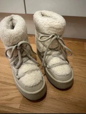 Vita fluffiga moon boots med snörning - Säljer ett par vita moon boots från H&M med fluffigt teddyfoder och bred snörning runt hela skon. De har en chunky sula och är perfekta för kalla dagar. .