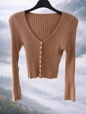 Brun ribbad kofta med pärlknappar - Trendig brun ribbad kofta med djup V-ringning och dekorativa pärlknappar framtill. Långärmad modell med smal passform och extra långa muddar. Perfekt att styla till jeans eller kjol för en snygg look.