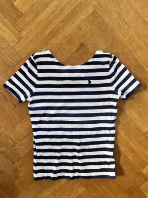 Randig T-shirt - Ralph Lauren - Så fin marinblå- och vitrandig T-shirt från Ralph lauren. Storlek barn  xl/16 år, passar en vanlig xxs-xs. Tröjan är i modellen boatneck och har lägre rygg än framsida. Inga defekter och bra skick.