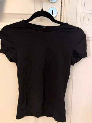 Svart basic t-shirt  - En enkel svart t-shirt med rund hals och korta ärmar. Perfekt för att matcha med jeans eller shorts. Materialet är mjukt och känns skönt mot huden, och passformen är normal. Snygg och stilren design utan mönster eller detaljer.