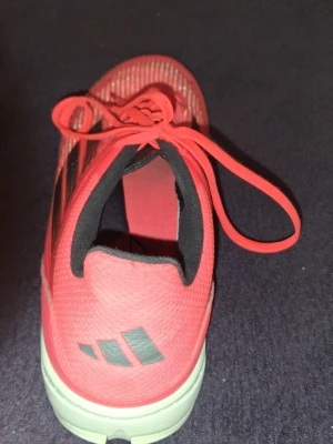 Röda Adidas sneakers med svarta ränder - Snygga röda sneakers från Adidas med klassiska svarta ränder på sidan och vit sula. Skon har en låg profil och är tillverkad i ett lätt, ventilerande material med svart vadderad insida. Perfekt för dig som gillar sportig stil och vill sticka ut.