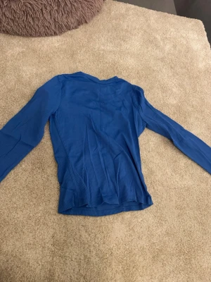 Blå ribbad långärmad topp - En enkel blå långärmad topp med ribbad struktur. Toppen har en smal passform och är tillverkad i ett mjukt, stretchigt material som känns bekvämt mot huden. Perfekt att styla med jeans eller kjol för en clean look.