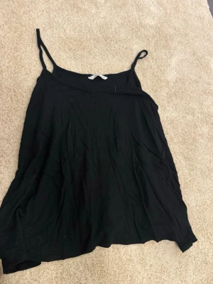 Svart linnetopp från Ellos - Säljer en enkel och stilren svart linnetopp från Ellos med tunna axelband. Toppen har en lös passform och är perfekt att matcha med jeans eller kjol. Materialet känns mjukt och lätt mot huden.