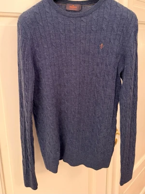 *MISSA INTE* kabelstickad tröja Morris - Kabelstickad blå tröja från Morris med rund halsringning och diskret logga broderad på bröstet. Tröjan har långa ärmar och ribbade muddar vid ärmslut och nederkant. Perfekt för lager på lager och klassisk stil. Pris kan diskuteras!