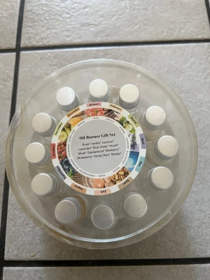 Oljebrännare presentset doftoljor - Säljer ett oljebrännare presentset med 12 små flaskor doftoljor i olika dofter som ros, vanilj, jasmin, lavendel, blå vatten, trä, mysk, sandelträ, blåbär, jordgubb, honung och mango. Flaskorna är genomskinliga med silverfärgade lock och kommer i en rund plastförpackning.