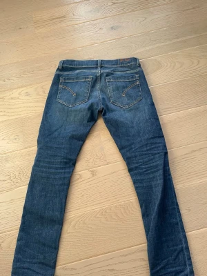 Blå raka jeans från Dondup  - Säljer ett par klassiska blå jeans från Dondup med raka ben och snygga kontrastsömmar. Jeansen har två bakfickor med dekorativa sömmar och bälteshällor. Perfekta för en stilren och avslappnad look. PRIS KAN DISKUTERAS 
