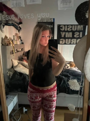 Röda julmönstrade pyjamasbyxor - Säljer ett par röda pyjamasbyxor med vitt julinspirerat mönster och text. Byxorna har resår i midjan och är perfekta för mysiga kvällar hemma. Materialet ser ut att vara mjukt och stretchigt, troligen bomull eller bomullsblandning.