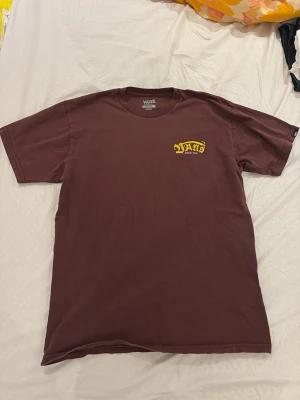 Brun Vans t-shirt med tryck - Säljer en brun t-shirt från Vans med gul och rosa logga på bröstet där det står 'Vans Since 1966'. Klassisk passform och rund halsringning. Perfekt för dig som gillar streetwear och vill ha en enkel men snygg tee.