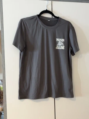 Grå t-shirt med tryck 'The Ocean is Calling' - Säljer en grå t-shirt med vit text och sköldpaddsmotiv där det står 'The Ocean is Calling' både fram och bak. T-shirten har rund hals och korta ärmar. Perfekt för dig som gillar havet och vill ha en chill look.