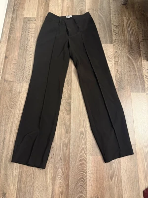 Svarta kostymbyxor från Madlady - Säljer ett par svarta kostymbyxor från Madlady i rak modell med pressveck. Byxorna har hällor för skärp och en klassisk midja. Perfekta för en clean och stilren look.