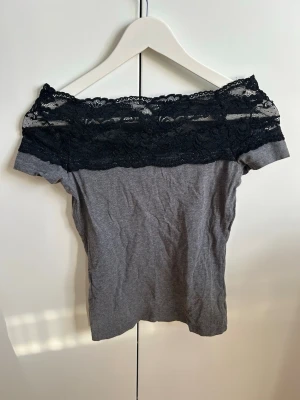 Grå offshoulder topp med svart spets - Snygg grå offshoulder topp med bred svart spets upptill. T-shirten har en figurnära passform