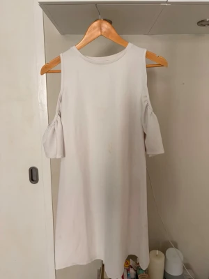 Vit kortklänning med cold shoulder - Stilren vit kortklänning med trendiga cold shoulder-ärmar och rund halsringning. Klänningen har en rak passform och är tillverkad i ett mjukt bomullsliknande material. Perfekt för dig som gillar minimalistisk och modern stil. 🥰🥰