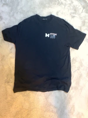 Svart Mysterious 333 t-shirt - Cool svart t-shirt från Mysterious med tryck fram och stort grafiskt tryck på ryggen. Framtill står det 'Mysterious 333' med en fjäril, och på ryggen finns en stor text och illustration. Klassisk passform och rund hals. Perfekt för dig som gillar streetwear vibes.