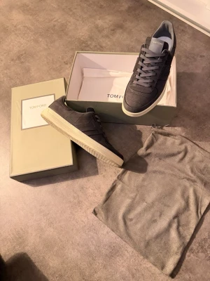 Tom Ford svarta sneakers i läder - Snygga svarta sneakers från Tom Ford i läder med diskret mönster och vita sulor. Klassisk låg modell med matchande svarta skosnören och perforerade detaljer på tån. Kommer med originalkartong och dustbag. Använd 1 gång