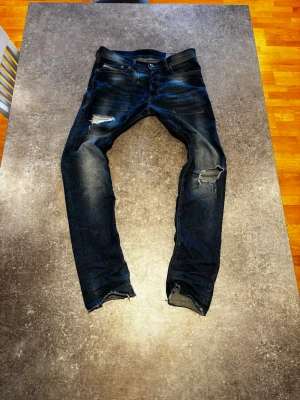 Diesel washed jeans  - Säljer ett par mörkblå jeans med slitningar och hål på både fram- och baksida. Jeansen har en smal passform och råa kanter vid bensluten. Perfekta för en avslappnad och trendig look. Materialet är klassisk denim i bomull.