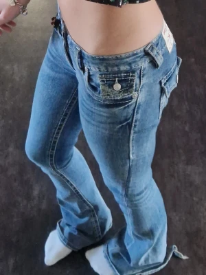 True Religion joey jeans  - Snygga lågmidjade och bootcut från true religion i modellen joey, har broderi på baksidan som är skitsnyggt! Har en del slitningar vid hälen(se bild) men de syns inte när jeansen är på!💕💕 utöver det väldigt bra skicka men de har använts så tecken på de finns såklart 🫰