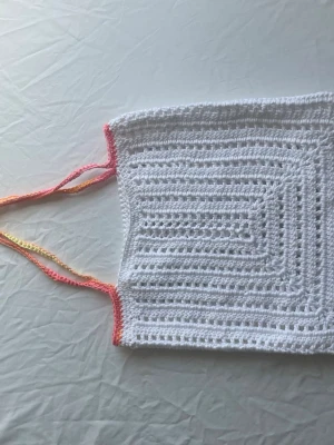 Handvirkad vit väska - Handvirkad väska i vitt garn med fyrkantig form och detaljerat mönster. Axelbanden är tunna och har en färgskiftning i rosa, orange och gult. Väskan är perfekt för somriga dagar. Materialet är bomulls garn.