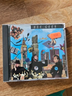 Bee Gees CD High Civilization - Säljer en CD-skiva med albumet 'High Civilization' av Bee Gees. Omslaget har färgglad collagekonst med stadsmotiv och figurer. Plastfodral med tryckt framsida och baksida där låtlistan syns. Perfekt för dig som gillar klassisk pop och samlar på musik.