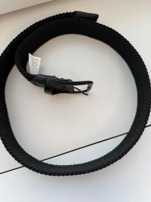 Helt nytt svart flätat stretchbälte från Up2 Fashion – 95 cm - Säljer ett helt nytt svart flätat stretchbälte från Up2 Fashion i storlek 95 cm. Den stilrena flätade designen i kombination med det elastiska materialet ger både hög komfort och en flexibel passform. Perfekt till jeans, chinos eller andra vardags- och festoutfits.  ✔ Helt nytt skick ✔ Färg: Svart ✔ Storlek: 95 cm ✔ Flätad design ✔ Stretchmaterial för optimal komfort ✔ Stilrent och lättmatchat  Kommer från ett djur- och rökfritt hem.  Kan skickas eller hämtas enligt överenskommelse.