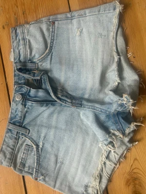 Ljusblå jeansshorts - Säljer ett par ljusblå jeansshorts med fransiga kanter och slitna detaljer. 