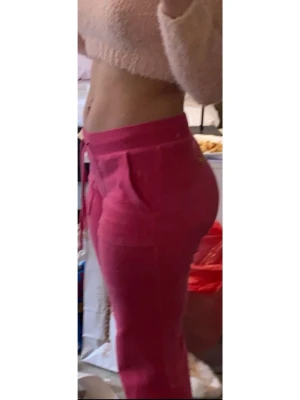 Mörkrosa Juicy Couture mjukisbyxor - Säljer ett par snygga rosa mjukisbyxor från Juicy Couture med hög midja och dragsko i midjan. Byxorna har fickor på sidorna och är gjorda i ett mjukt, bekvämt material. 