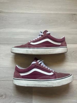 Vinröda Vans sneakers - Säljer ett par klassiska Vans Old School sneakers i vinrött med vit sula och vit sidostripes. Skorna har ovandel i mocka och canvas, vita skosnören och den ikoniska gummisulan med våffelmönster. Perfekta för en avslappnad streetwear-look.