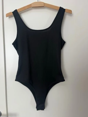 Svart ribbad body - Svart body med breda axelband och rundad urringning. Materialet är ribbat vilket ger en snygg struktur och extra komfort. Storlek M