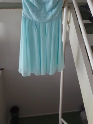 Ljusblå axelbandslös kortklänning - Söt ljusblå axelbandslös klänning med plisserad kjol och små vita pärldetaljer upptill. Klänningen har en luftig och flowy känsla, perfekt för somriga fester. 