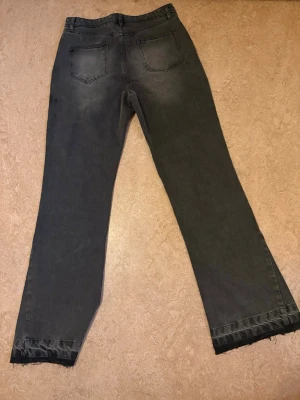 Svarta raka jeans med rå kant by Zara - Säljer ett par svarta jeans med rak passform och rå, fransig kant nedtill. Jeansen har klassisk femficksdesign och subtila slitningar framtill för en avslappnad look. Perfekta för dig som gillar en enkel men trendig stil.